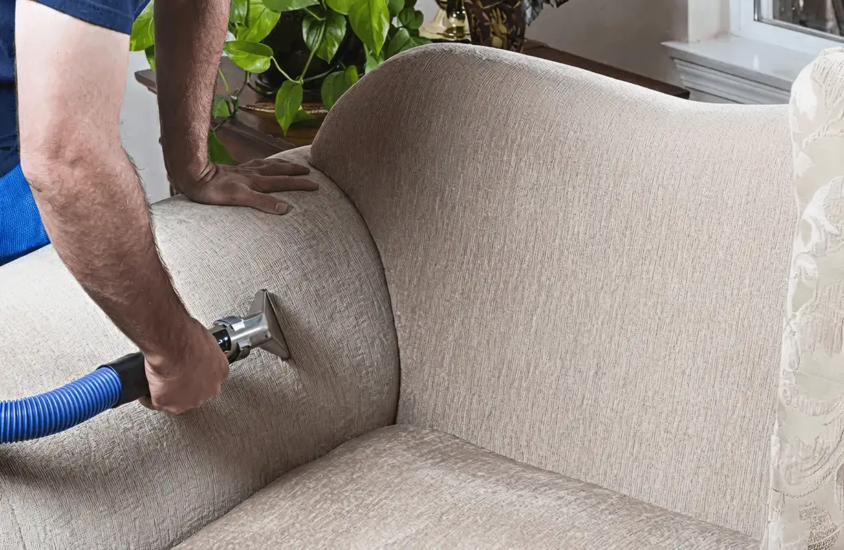 Professional upholstery cleaner deep-cleaning a fabric sofa with a handheld extraction tool and hose, Jersey City, NJ.